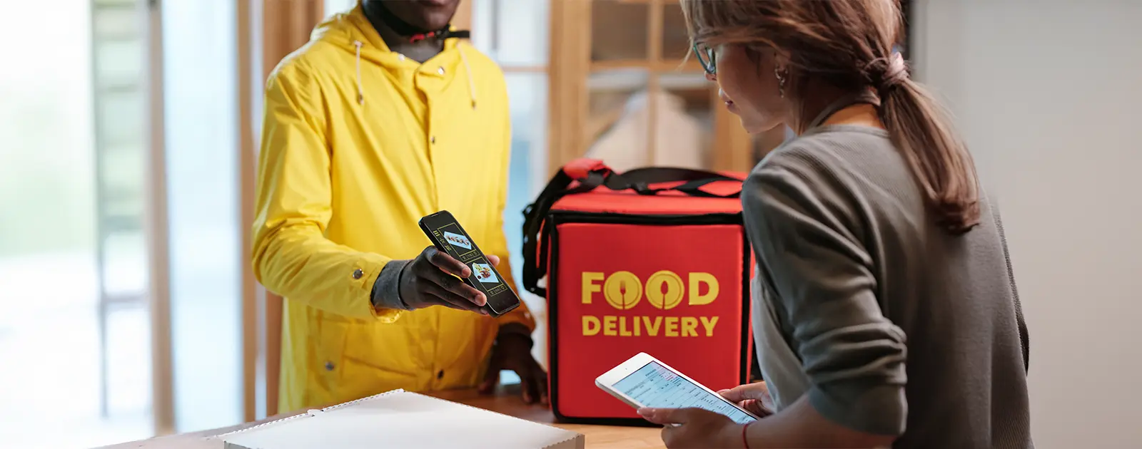 Entregador mostra celular a uma mulher com tablet em um balcão de delivery.